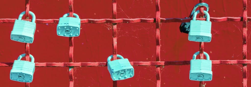 Padlocks on a fence in front of a red wall